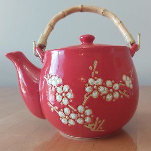 Red teapot with cherry blossom design in white with tan accent bamboo handle